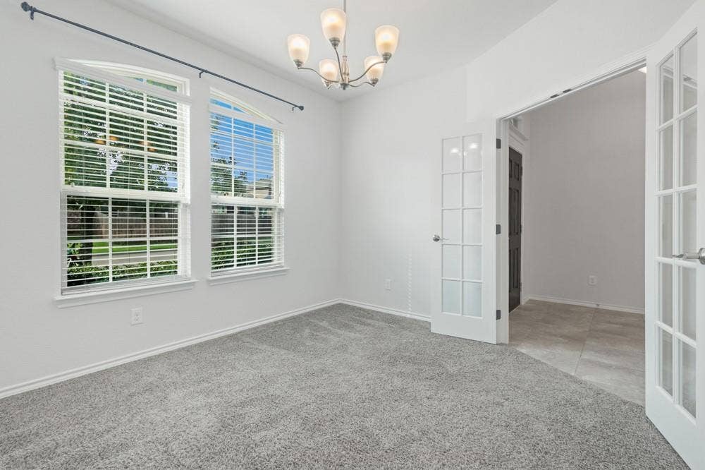 Room featuring carpeted flooring, arched windows, multi-pane French doors, and a five-light chandelier
