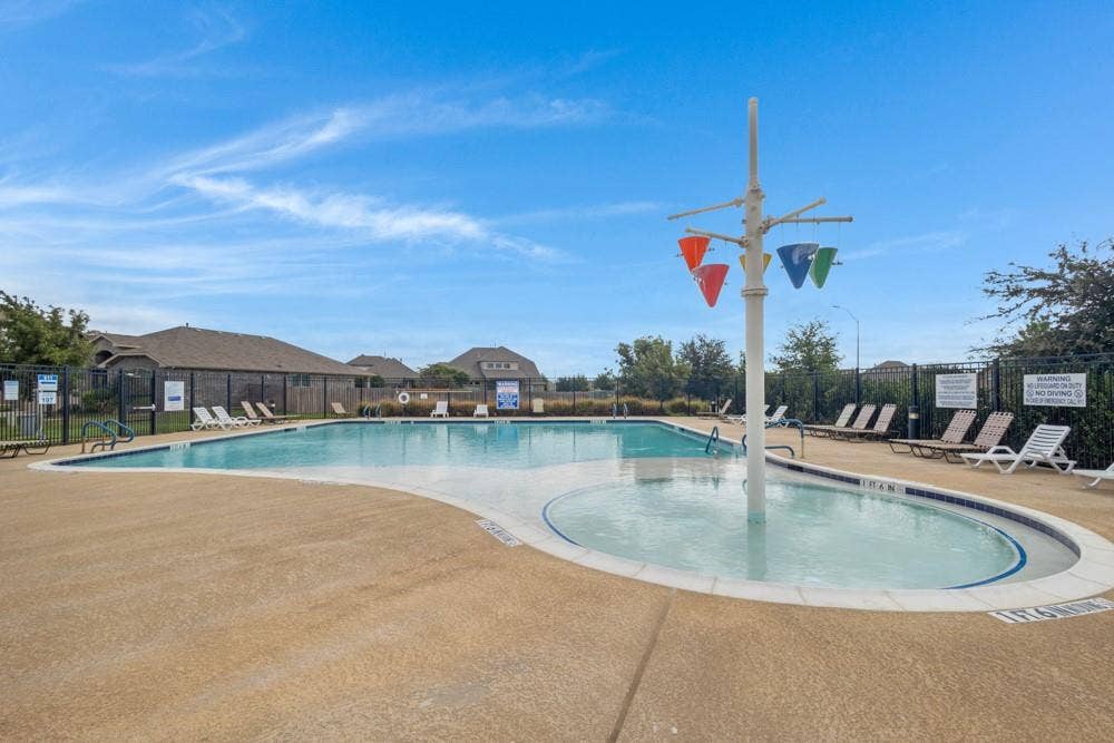 Swimming pool featuring a dedicated splash area with an overhead water feature and textured concrete decking enclosed by perimeter fencing