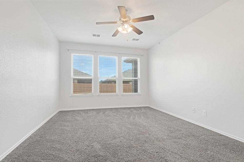 Neutral-toned interior room featuring wall-to-wall carpeting, three windows with horizontal blinds, and a ceiling fan with integrated lighting