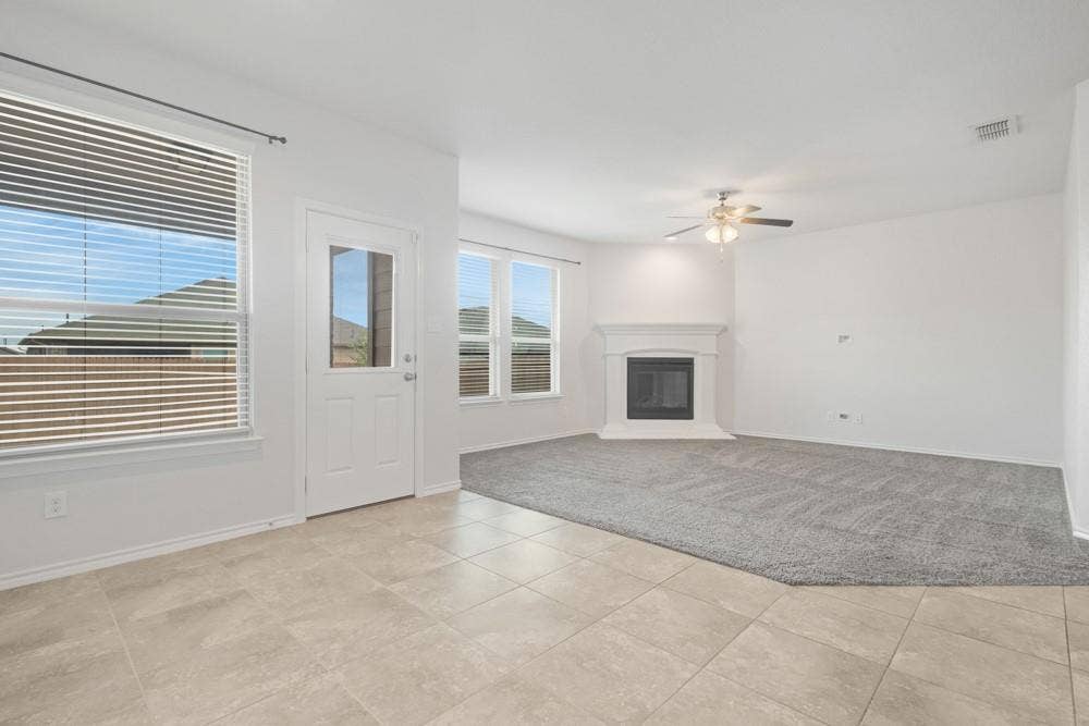 Open-concept interior featuring large-format tile flooring, plush carpeting, a corner fireplace with a mantel, and a ceiling fan