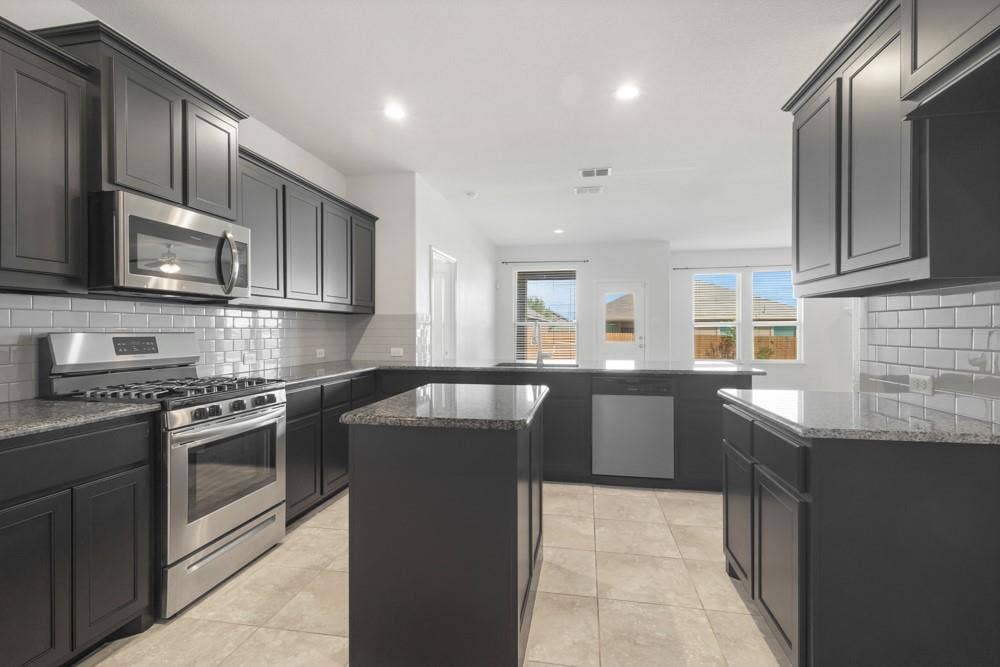 Kitchen featuring dark cabinetry, stone countertops, stainless steel appliances, a subway tile backsplash, and a central island