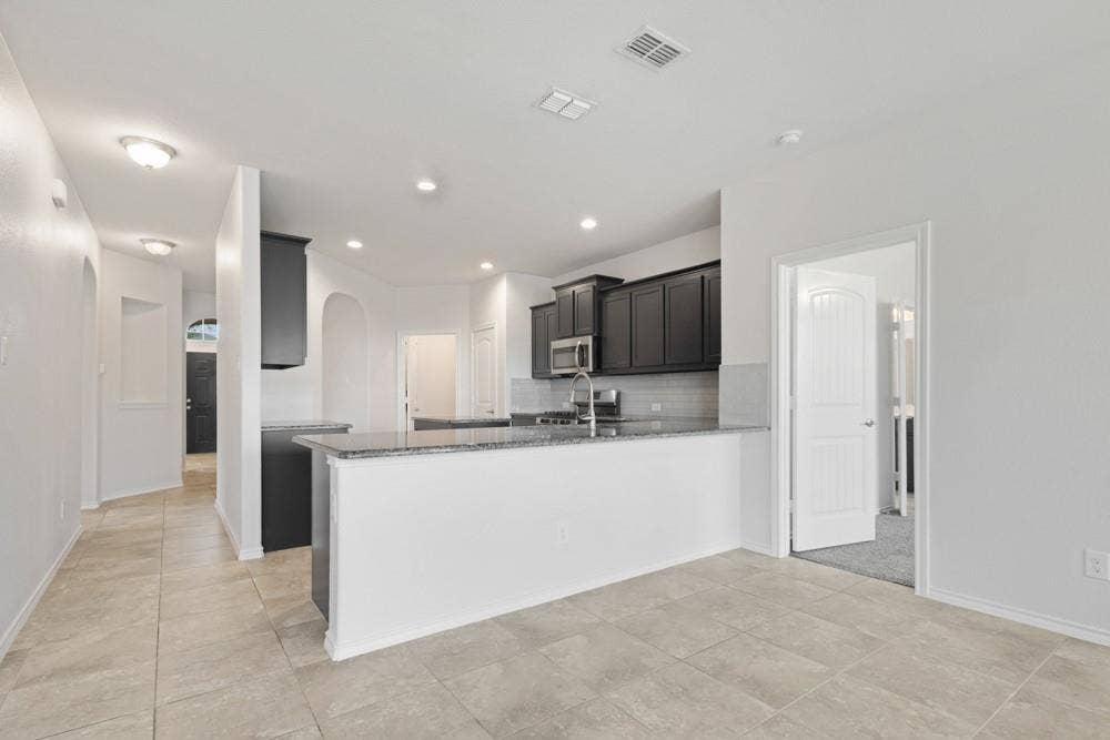 Kitchen featuring dark cabinetry, stone-surface countertops, tile flooring, recessed lighting, and a peninsula with a stainless steel undermount sink