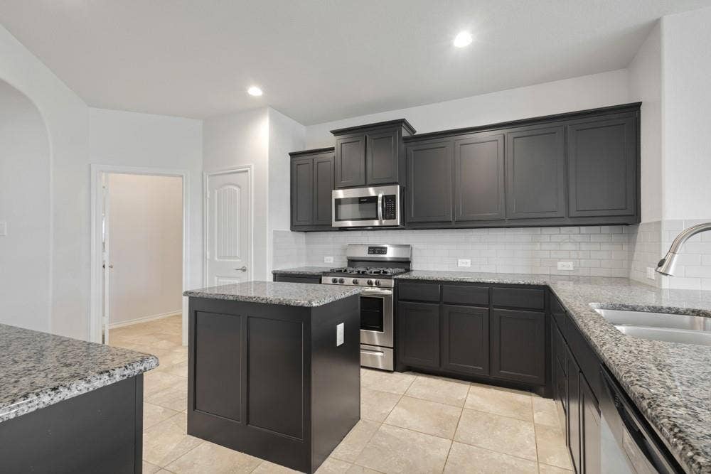 Kitchen featuring dark shaker-style cabinetry, stone countertops, stainless steel appliances, a center island, and a subway tile backsplash