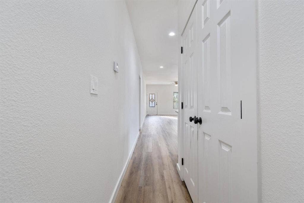 3023 Spurlock Street, Dallas, TX 75223 Hallway featuring wood-finish flooring, white textured walls, recessed ceiling lighting, and a six-panel closet door with black hardware