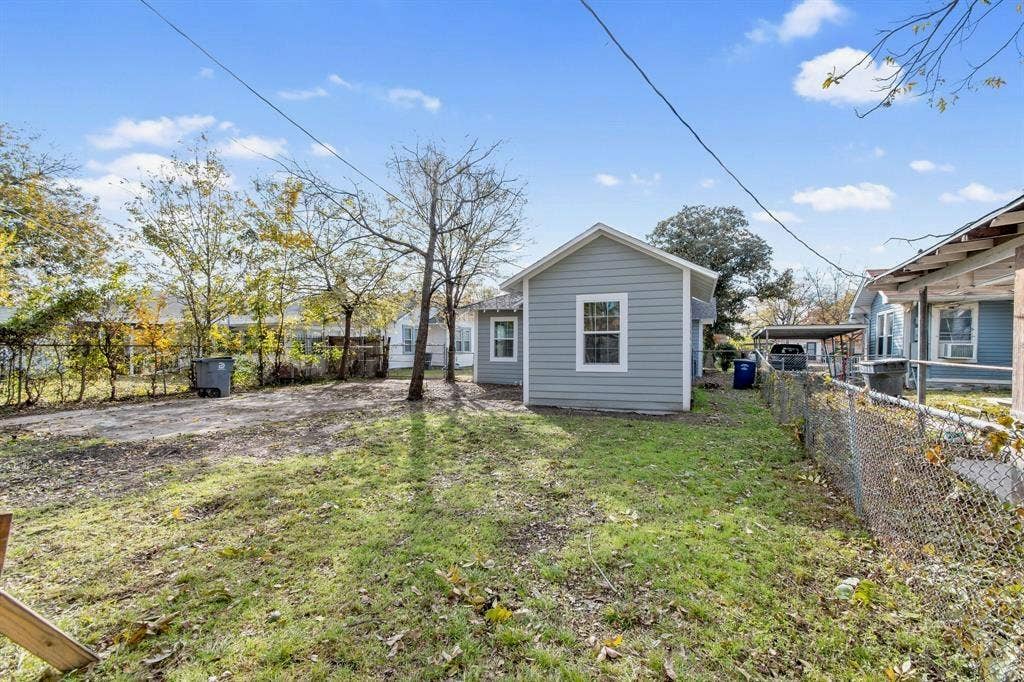 3023 Spurlock Street, Dallas, TX 75223 Exterior features include horizontal lap siding, a metal chain-link perimeter fence, and mature trees situated on a level lot
