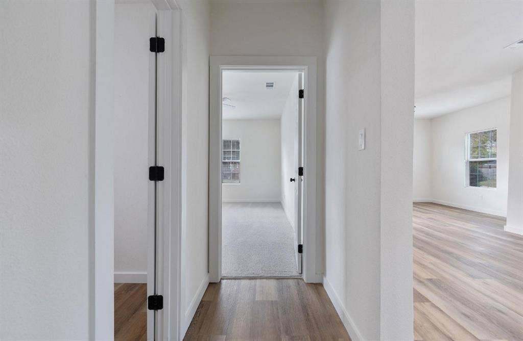 3023 Spurlock Street, Dallas, TX 75223 Interior hallway featuring neutral-toned wall paint, wood-finish flooring, and doorways accented with matte black hinges