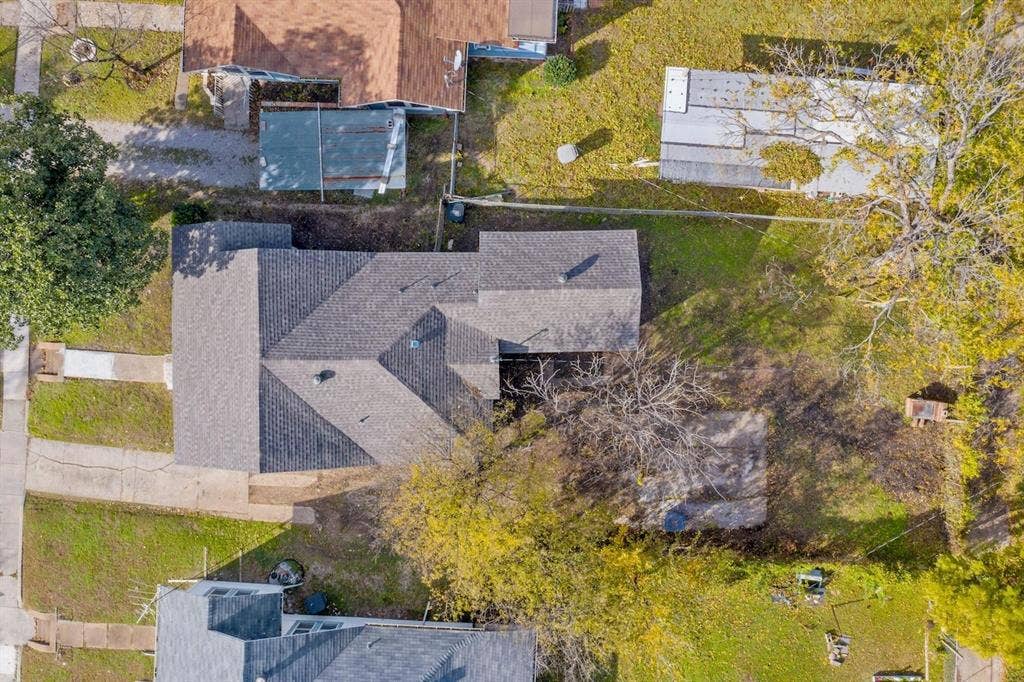 3023 Spurlock Street, Dallas, TX 75223 Aerial perspective featuring an asphalt shingle roof, paved driveway, expansive lawn, and mature trees