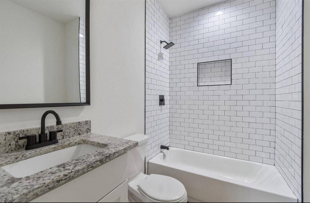 3023 Spurlock Street, Dallas, TX 75223 Bathroom featuring a stone-look countertop, undermount sink, matte black faucet and fixtures, and a shower-tub combination with white subway tile surround and a recessed niche