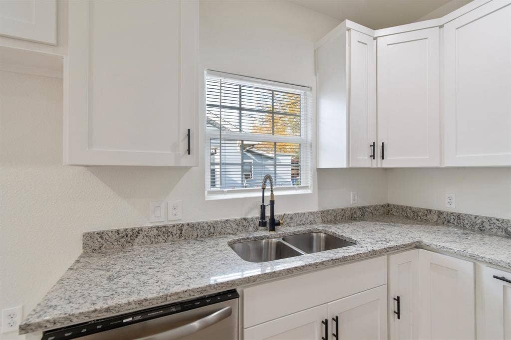 3023 Spurlock Street, Dallas, TX 75223 Kitchen featuring white shaker-style cabinetry, speckled stone countertops, dual-basin stainless steel sink, matte black gooseneck faucet, and stainless steel dishwasher