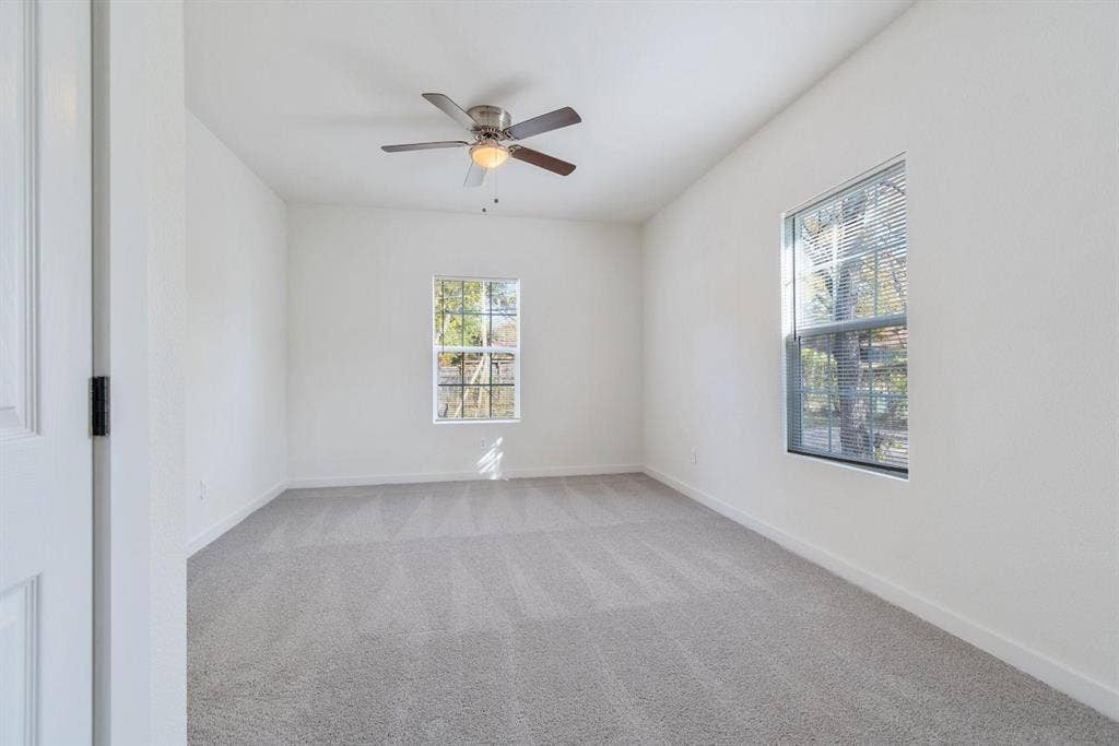 3023 Spurlock Street, Dallas, TX 75223 Neutral-toned carpeted interior featuring a ceiling fan with integrated lighting and two windows with horizontal blinds