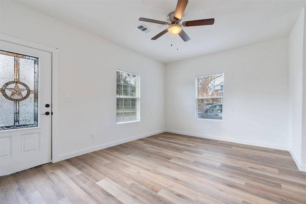 3023 Spurlock Street, Dallas, TX 75223 Interior room featuring wood-finish flooring, two dual-pane windows, a ceiling fan with integrated lighting, and an exterior door with a decorative glass insert