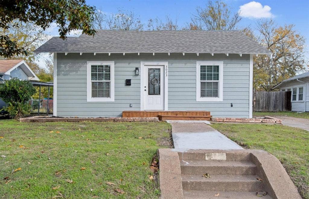 3023 Spurlock Street, Dallas, TX 75223 Single-story residence featuring horizontal siding, a gabled roofline, an elevated wood-plank porch, and a concrete walkway