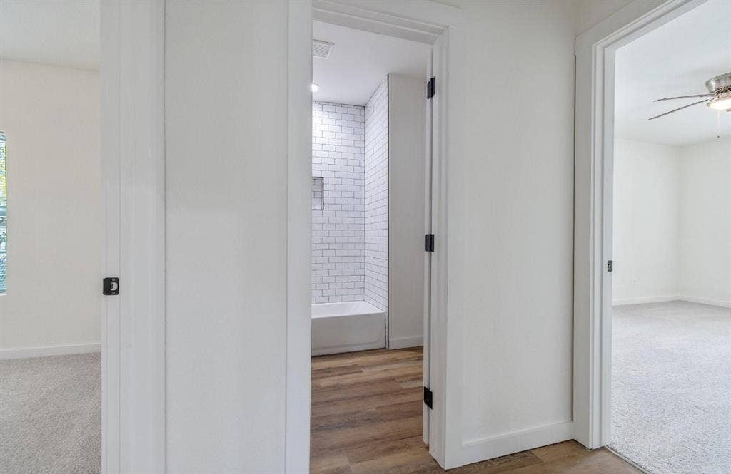 3023 Spurlock Street, Dallas, TX 75223 Interior featuring white subway tile shower surround with recessed niche, wood-finish flooring, and black hardware accents on crisp white doors