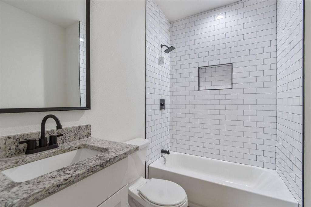 3023 Spurlock Street, Dallas, TX 75223 Bathroom featuring a vanity with a stone-finish countertop, white subway tile shower surround with integrated wall niche, matte black fixtures, and a framed mirror