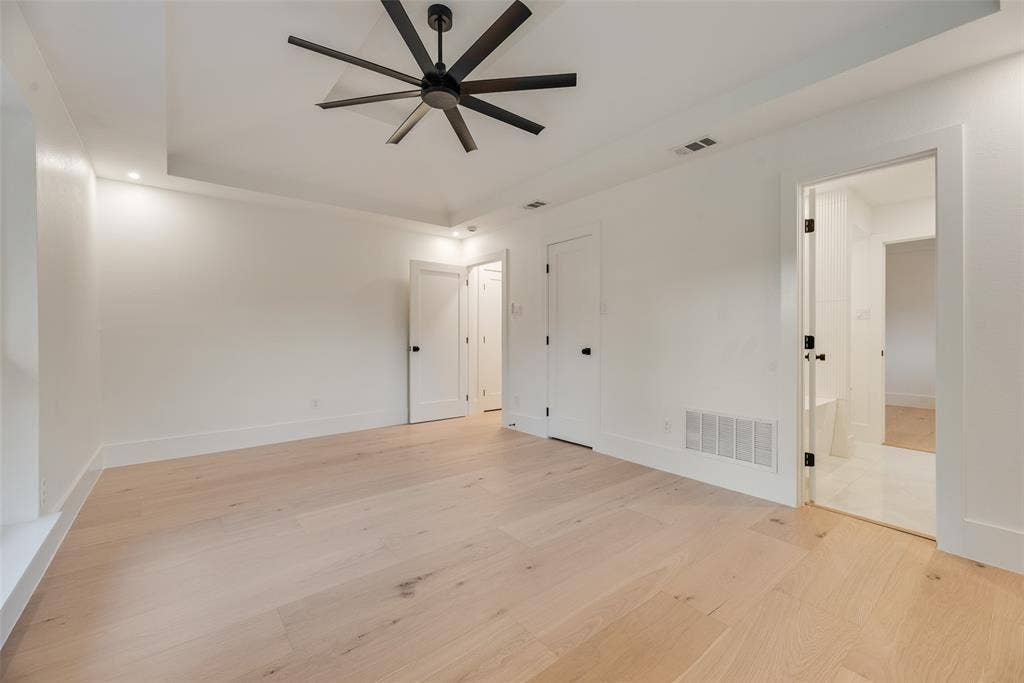 Tray ceiling, wood-finish flooring, and multi-blade matte black ceiling fan