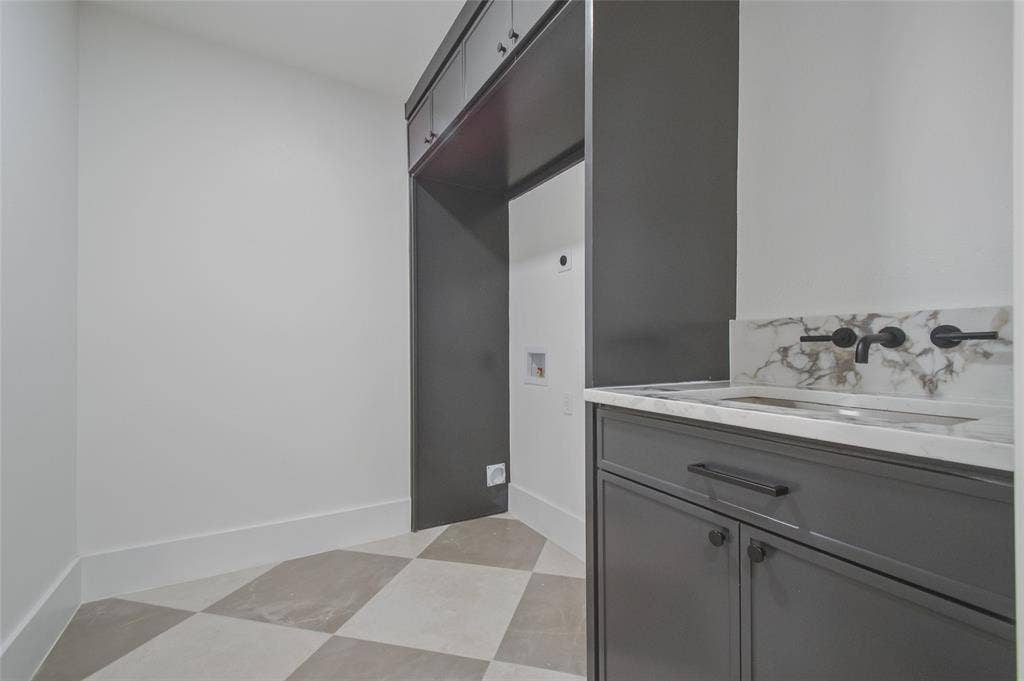 Dark gray built-in cabinetry, stone-finish countertop with integrated sink, matte black wall-mounted faucet, and geometric tile flooring