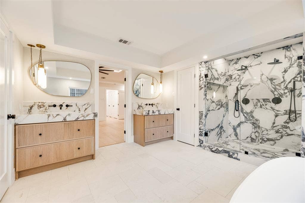 Dual vanities featuring fluted wood cabinetry, patterned stone countertops, and organic-shaped mirrors
