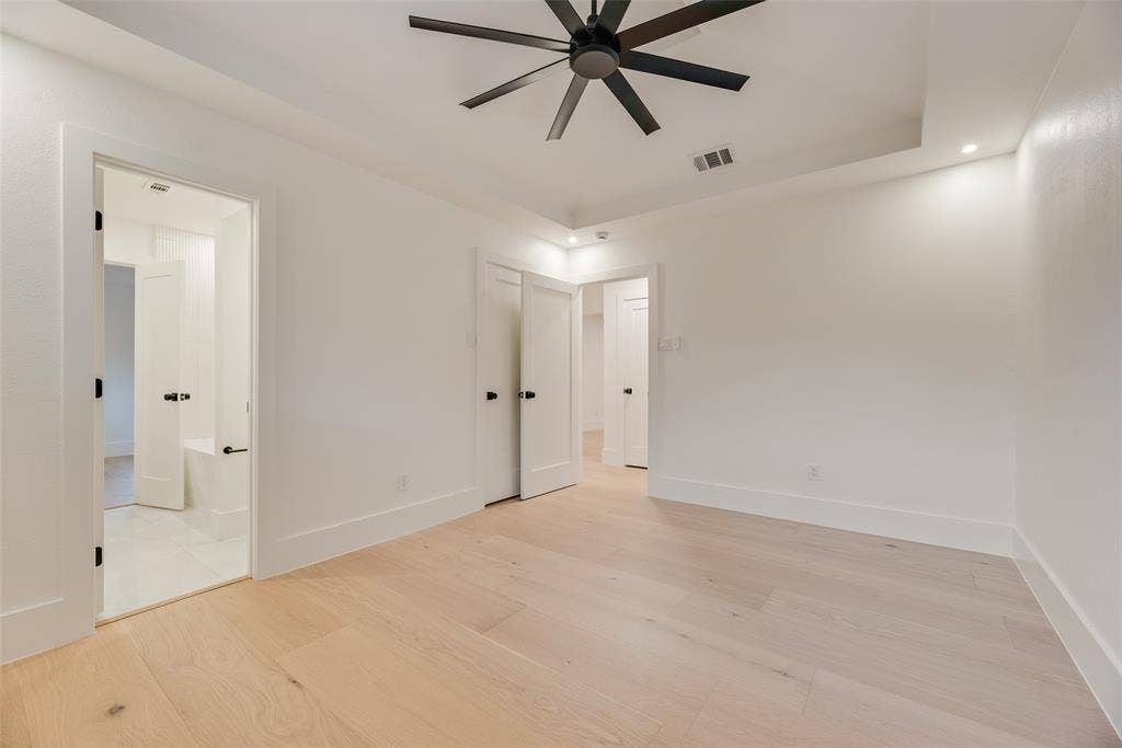 Room featuring wood-finish flooring, tray ceiling, recessed lighting, and a matte black ceiling fan