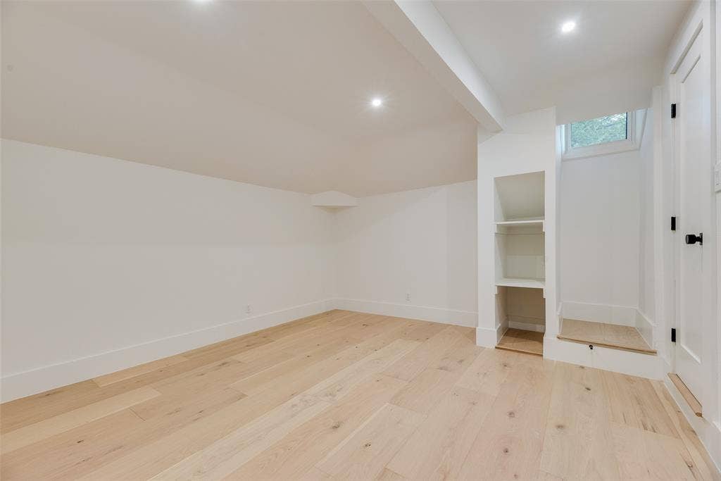 Vaulted ceilings, wood-finish flooring, recessed lighting, built-in shelving, and a single-panel door with matte black hardware