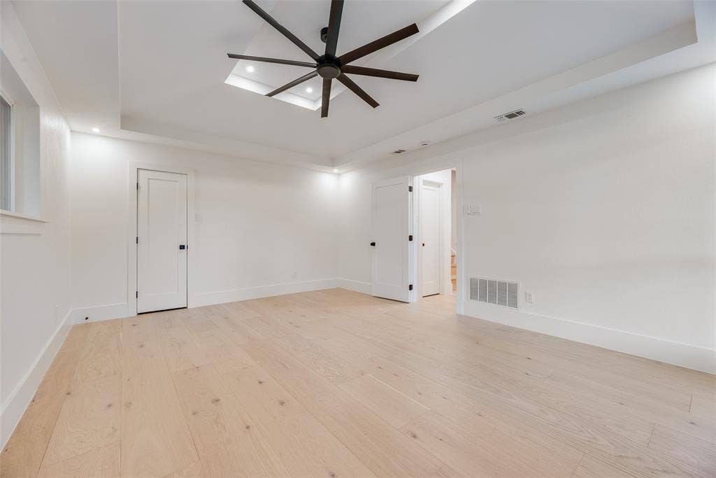 Tray ceiling featuring recessed lighting and a multi-blade ceiling fan, light-toned wood-finish flooring, and solid-core interior doors with matte black hardware