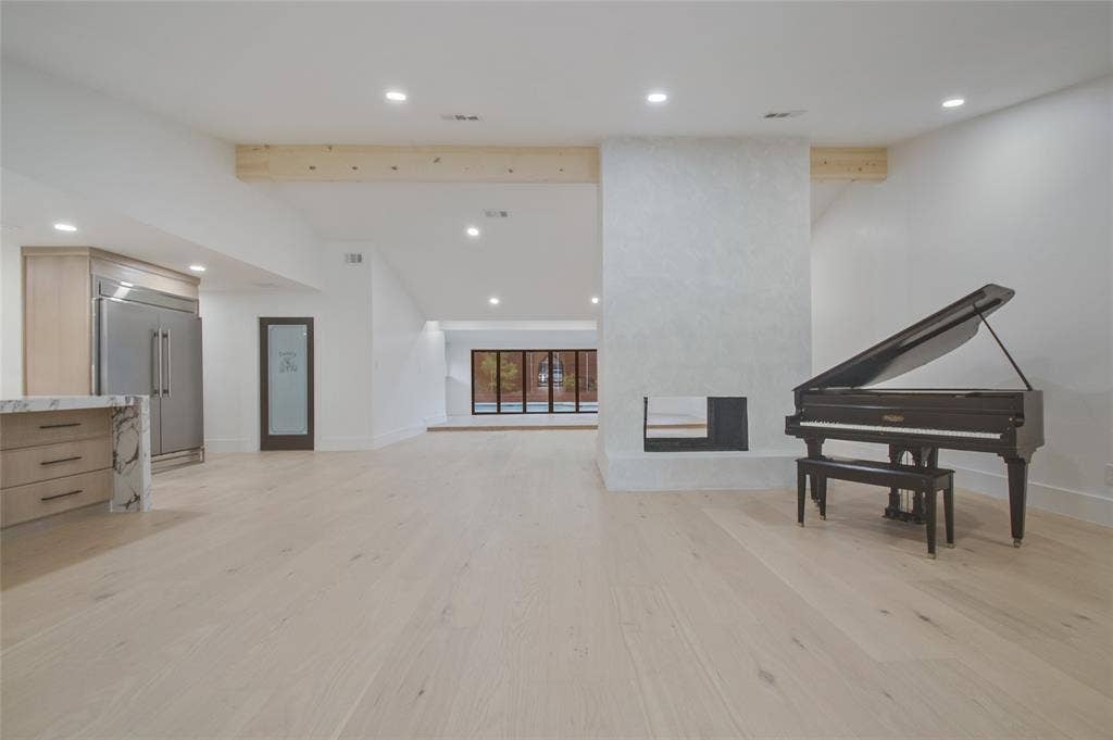 Open-concept living space featuring wood-finish flooring, recessed lighting, exposed structural beams, a central fireplace with a smooth plaster finish, and built-in cabinetry with stone-finish countertops