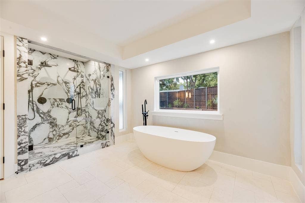 Walk-in shower with floor-to-ceiling stone-patterned tile, frameless glass enclosure, freestanding soaking tub, matte black plumbing fixtures, and recessed lighting