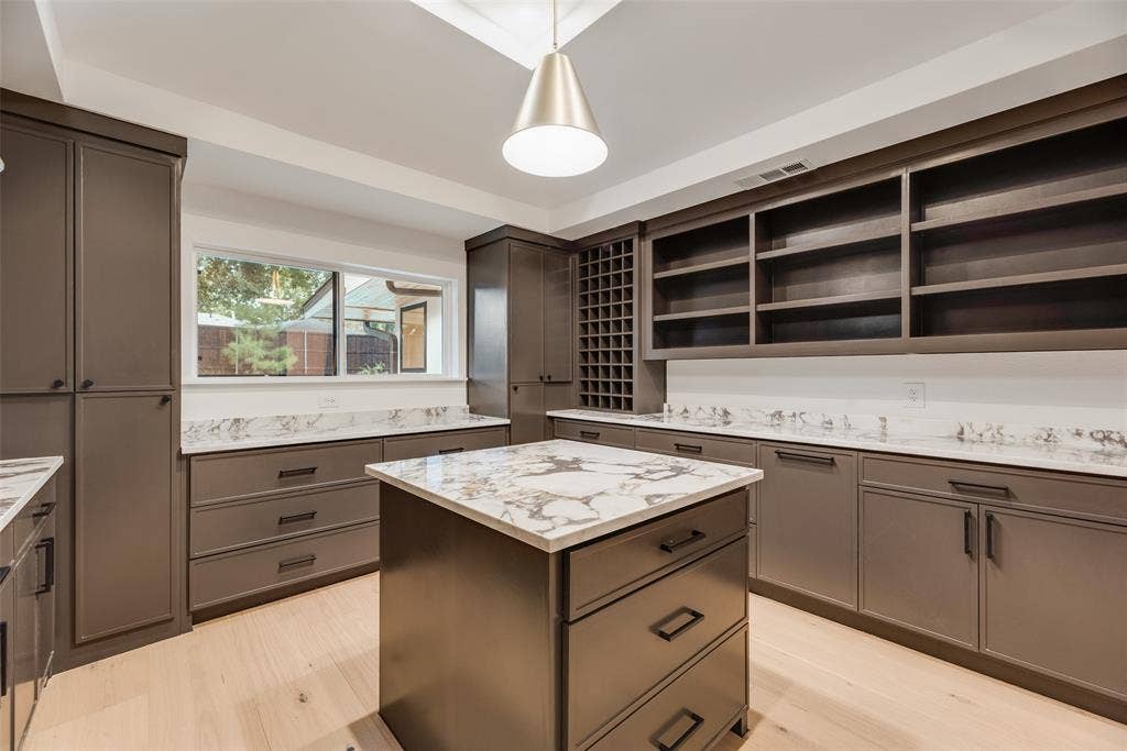 Custom cabinetry with integrated wine storage, stone countertops, central island, wood-finish flooring, and pendant lighting
