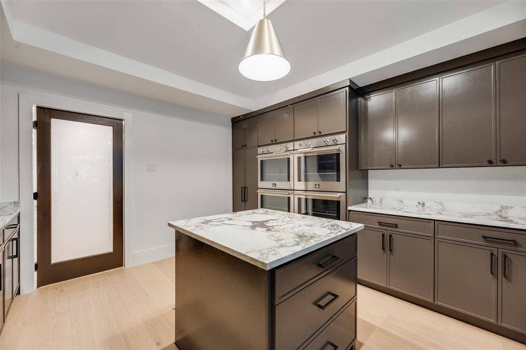 Kitchen featuring dark cabinetry, stone-surface countertops, built-in double wall ovens, a central island, and a frosted glass door