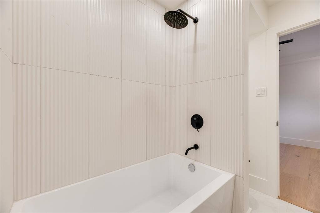 Full-height vertical fluted wall tiling surrounding a white soaking tub with matte black fixtures, including a round rainfall shower head and wall-mounted tub faucet