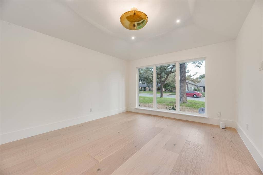 Interior space featuring light-toned wood-finish flooring, high tray ceiling, large picture window, and a modern gold-finish semi-flush mount light fixture