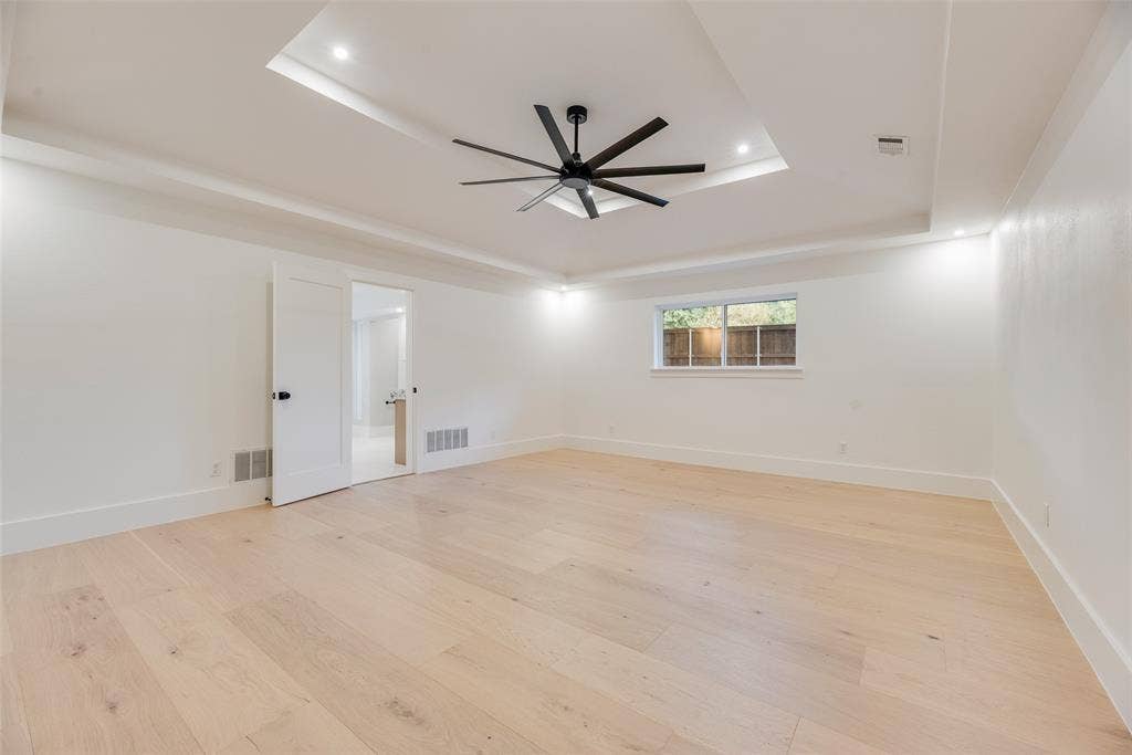 Tray ceiling with recessed lighting, matte black multi-blade ceiling fan, wood-finish flooring, and shaker-style interior door