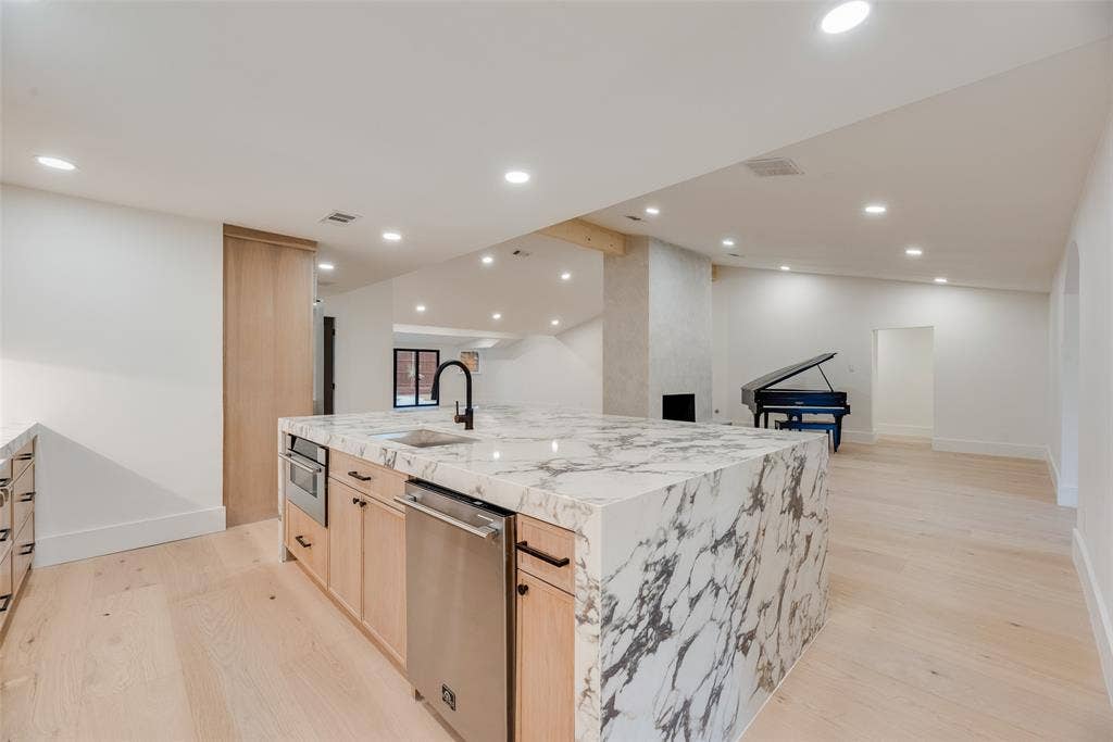 Kitchen featuring a waterfall-edge island with stone countertop, light wood-finish cabinetry, stainless steel dishwasher, matte black faucet, and recessed lighting