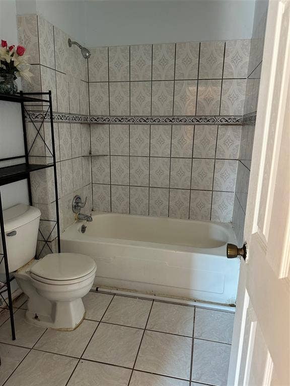 Full bathroom featuring a tub-and-shower combination, patterned wall tile with decorative border accent, and ceramic floor tiling