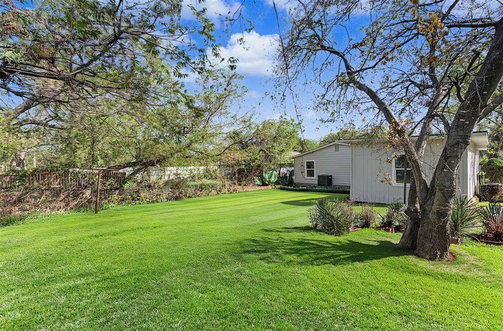Spacious backyard featuring a manicured lawn, mature trees, and a perimeter fence