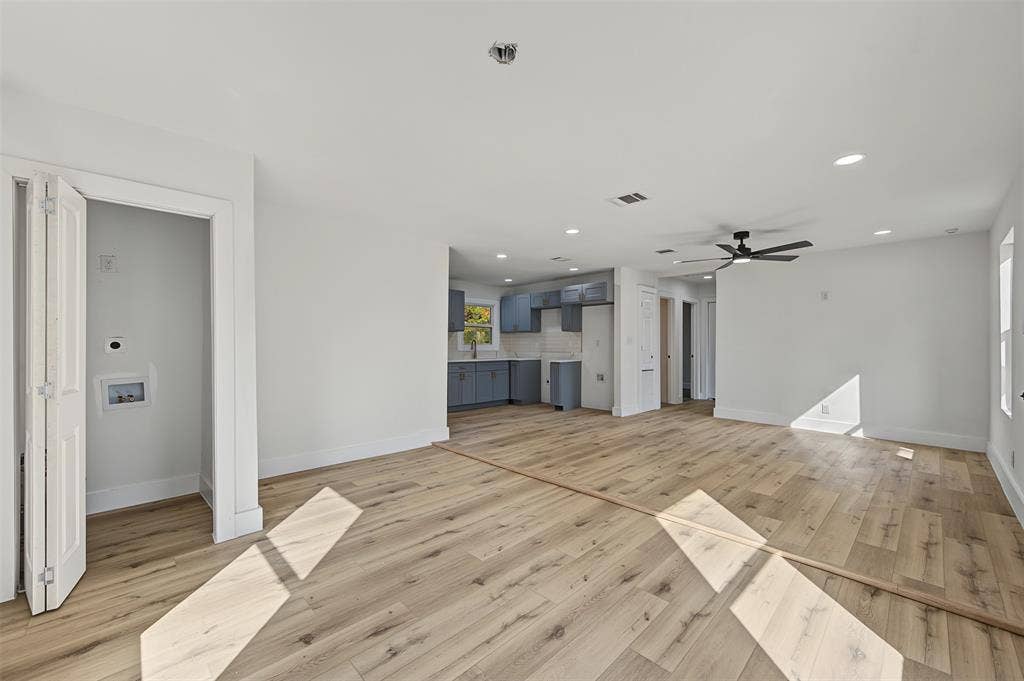 Open-concept interior featuring light-tone wood-finish flooring, recessed lighting, a matte black ceiling fan, and built-in laundry closet with bi-fold doors
