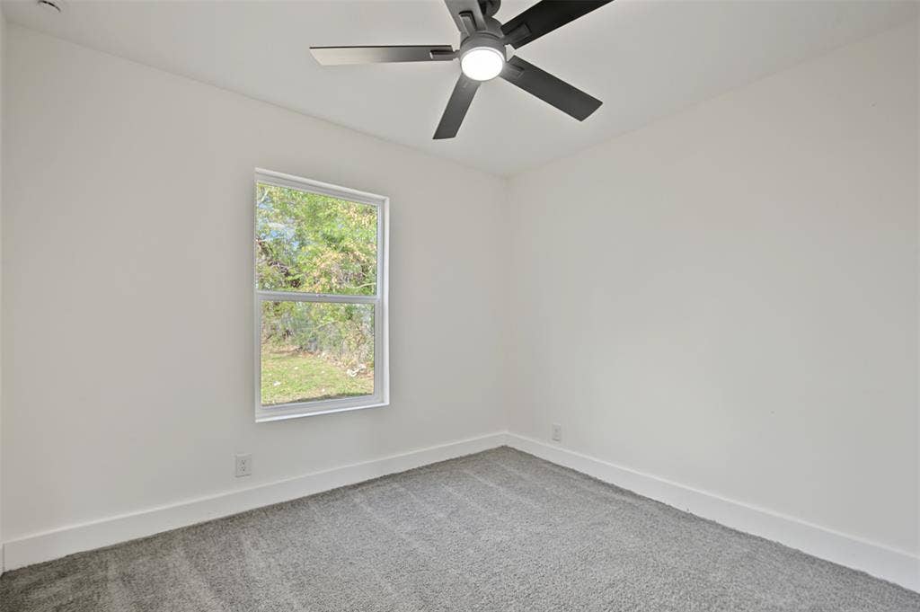 Neutral-toned interior featuring grey wall-to-wall carpeting, white walls, a single-hung window, and a matte black ceiling fan with integrated LED lighting