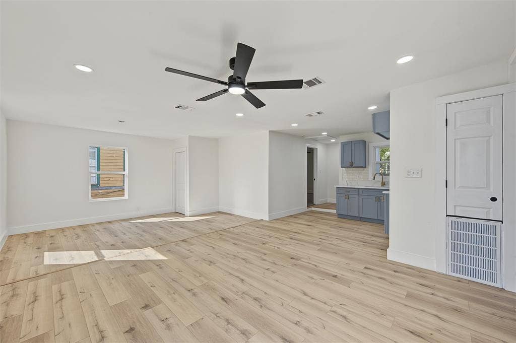 Open-concept interior featuring light wood-finish flooring, recessed lighting, a matte black ceiling fan, and cabinetry with quartz countertops