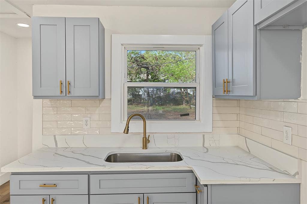 Kitchen featuring Shaker-style cabinetry, patterned stone-finish countertops, subway tile backsplash, stainless steel undermount sink, and brass-finish hardware