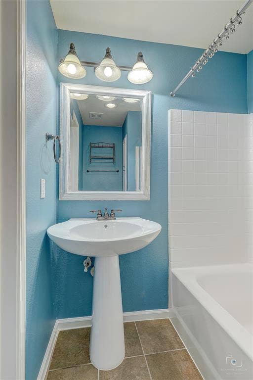 White pedestal sink with a dual-handle faucet, framed wall-mounted mirror, three-light vanity fixture, and tiled tub surround