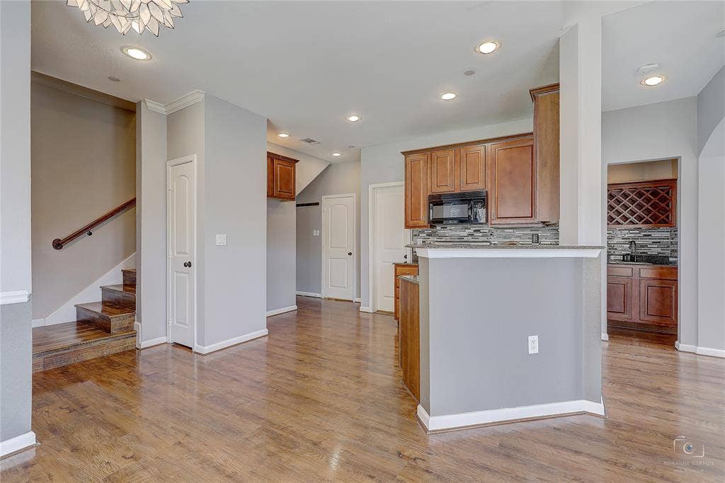 Wood-finish flooring, recessed lighting, stained wood cabinetry, stone-tile backsplash, and built-in wine storage
