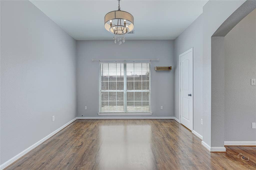 Wood-finish flooring, neutral wall tones, multi-light drum chandelier with crystal accents, large window with horizontal blinds, and built-in wall shelving