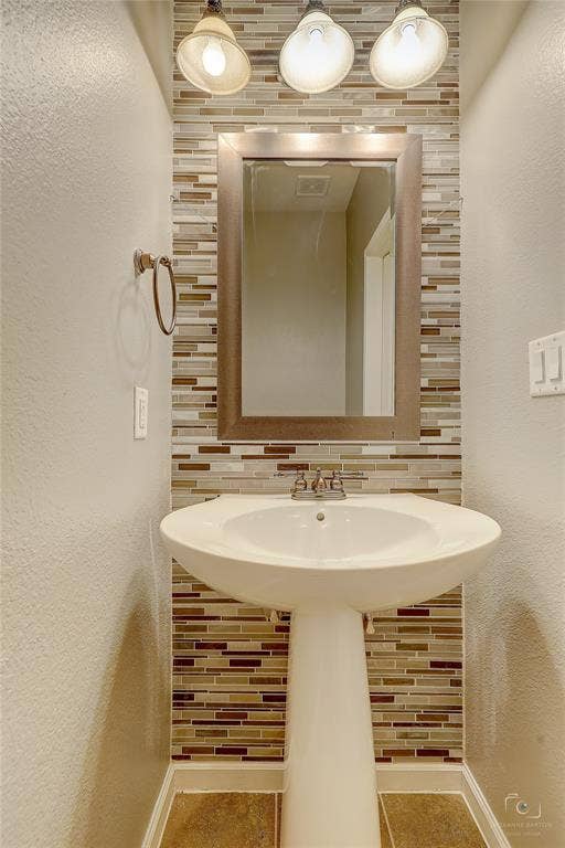 Pedestal sink with a metal faucet, linear tile backsplash, framed wall mirror, and a three-light fixture