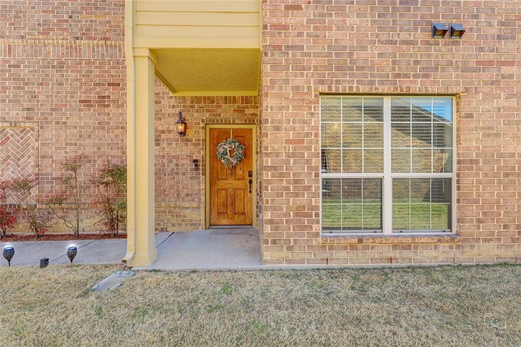Brick exterior featuring a recessed entry, wood-finish front door, large multi-pane window, and exterior wall-mounted lighting