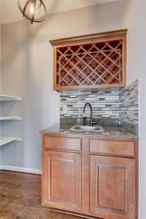 Custom cabinetry featuring built-in lattice wine storage, stone countertop, undermount sink, matte black faucet, and horizontal glass tile backsplash
