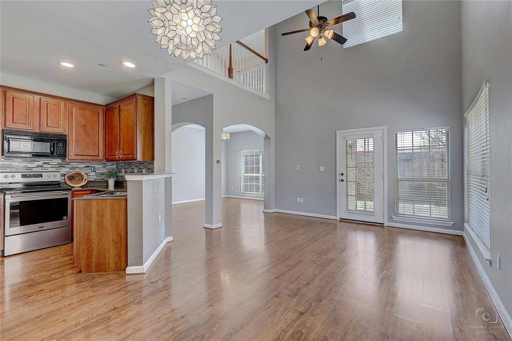 Double-height ceilings, wood-finish flooring, wooden cabinetry, integrated stainless steel appliances, and a decorative chandelier