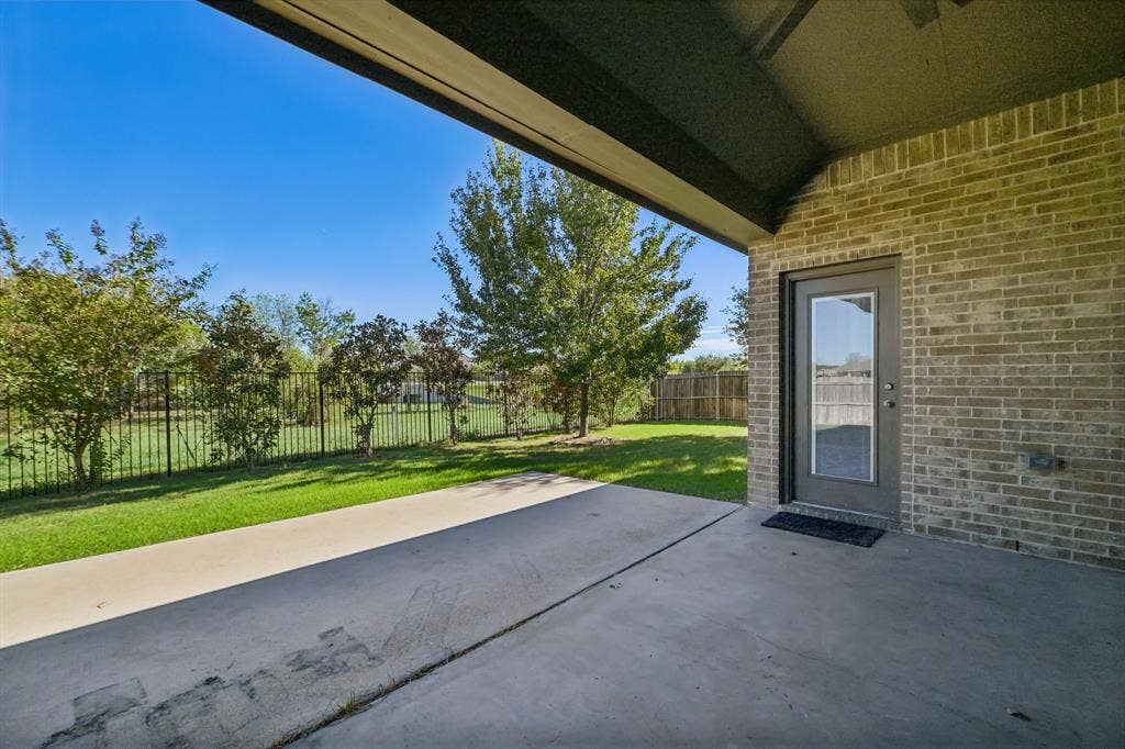 284 Goliad Trail, Forney, TX 75126 Covered concrete patio featuring brick exterior siding, a full-glass inset door, metal perimeter fencing, and mature landscaping