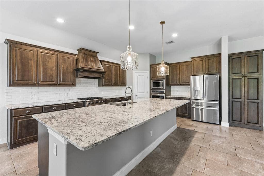 284 Goliad Trail, Forney, TX 75126 Kitchen featuring custom-stained cabinetry, stone countertops, a large center island, stainless steel appliances, and subway tile backsplash