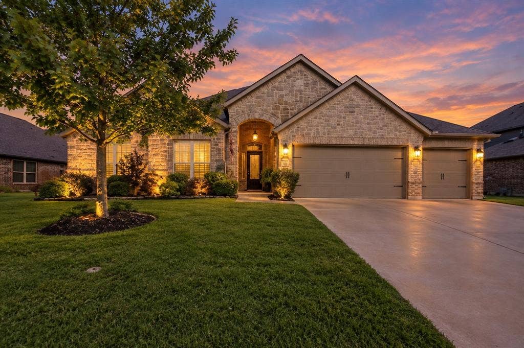 284 Goliad Trail, Forney, TX 75126 Stone masonry exterior, arched entryway, multi-car garage, concrete driveway, and manicured landscaping