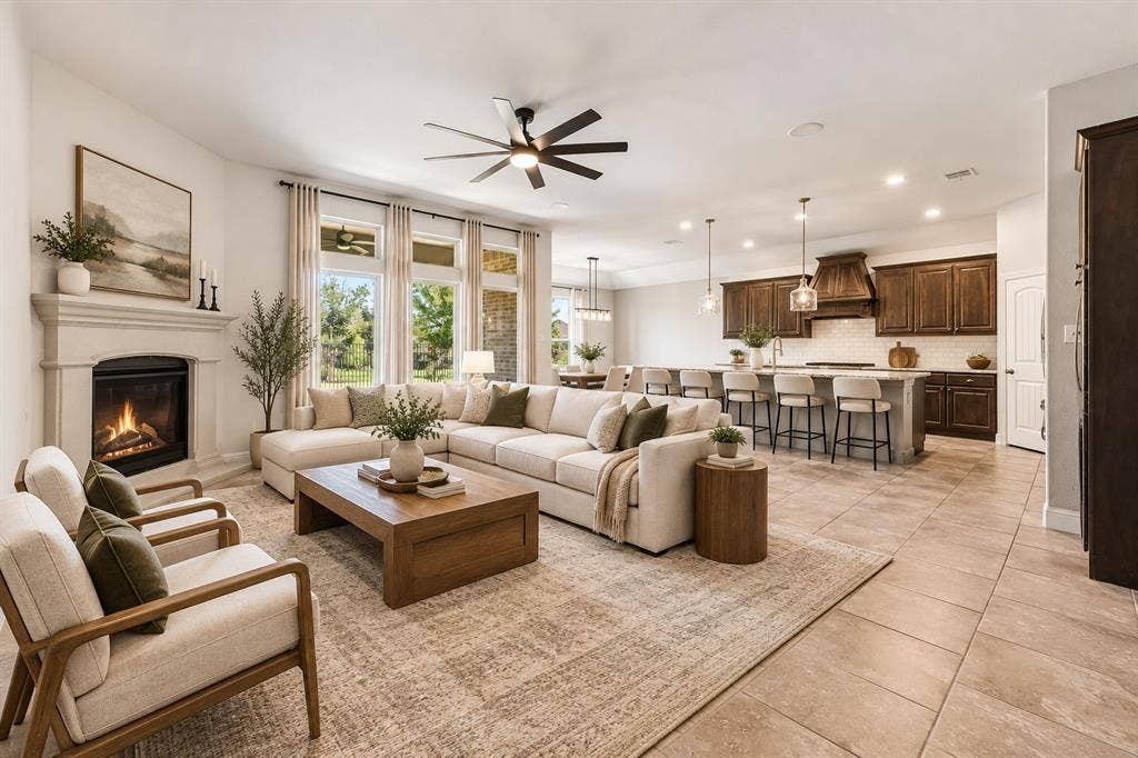 284 Goliad Trail, Forney, TX 75126 Open-concept interior featuring large-format tile flooring, a fireplace with a decorative mantel, tall windows, a kitchen island with stone countertops, and dark wood-finish cabinetry