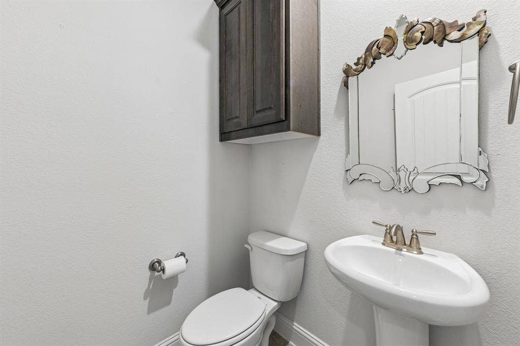 284 Goliad Trail, Forney, TX 75126 Wall-mounted dark wood-finish cabinet, pedestal sink with metallic two-handle faucet, and decorative arched wall mirror